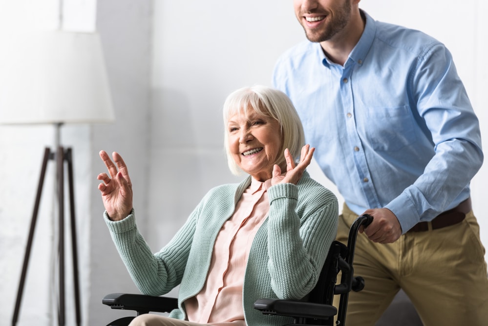 Young man pushing smiling senior woman in wheelchair