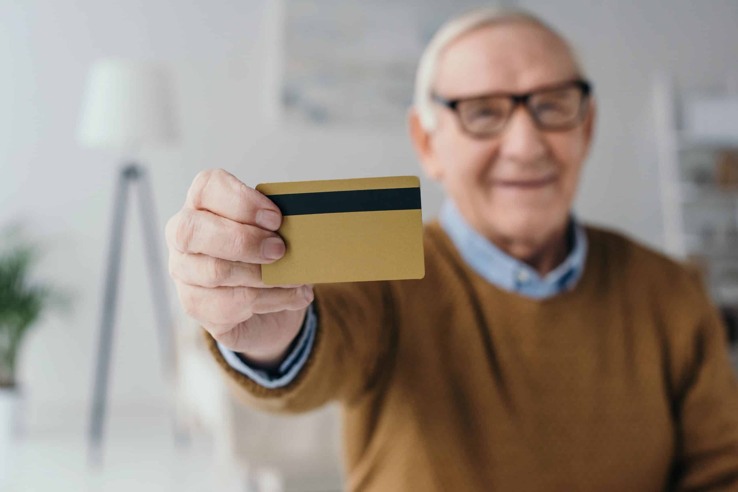 Senior man smiling and holding up credit card